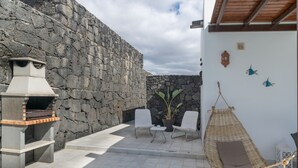 A stone wall, a grill, two chairs, a hanging chair, and a potted plant. - Vacation Villa 'Kalima' with Mountain View, Wi-Fi and Air Conditioning (Playa Blanca)