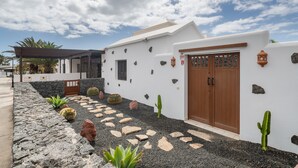 A white building with a stone wall, a wooden door, and a cactus garden. - Vacation Villa 'Kalima' with Mountain View, Wi-Fi and Air Conditioning (Playa Blanca)