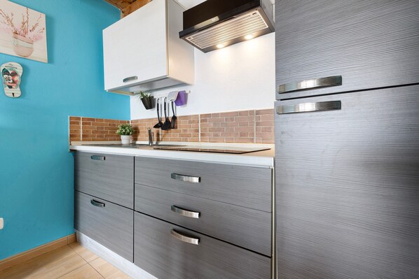 Une cuisine au design moderne, dotée d’un réfrigérateur en acier inoxydable, de meubles de couleur grise, d’un mur de fond en briques et d’un mur bleu.