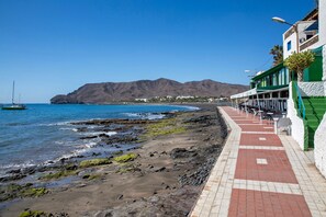 Une promenade en bord de mer avec un restaurant, une plage rocheuse et des montagnes en arrière-plan.