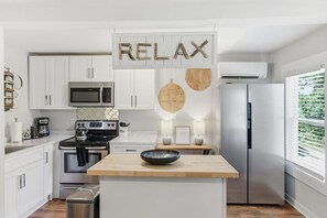 Een moderne keuken met witte kasten, een roestvrijstalen koelkast, een magnetron en een houten kookeiland met een kom.