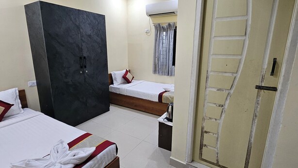 Une chambre d’hôtel avec deux lits, une armoire, une porte et une paire de chaussons posés sur le sol.