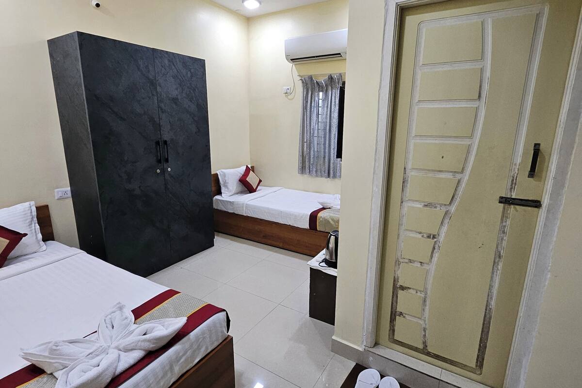A hotel room with two beds, a wardrobe, a door, and a pair of slippers on the floor.