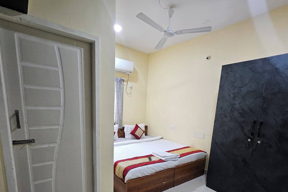 A bedroom with a bed, a wardrobe, a ceiling fan, and a pair of slippers on the floor.