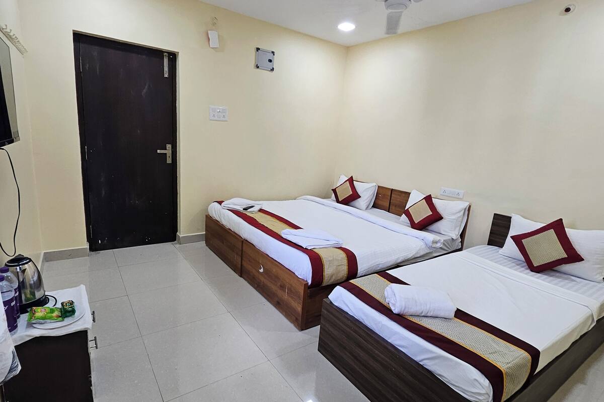 A hotel room with two beds, a ceiling fan, a small table with a kettle and snacks, and a door.