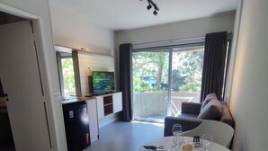 A modern living room with a dining area, a kitchen, and a balcony with a view of greenery. - APARTAMENTO MEU LAR LIBERDADE SP (São Paulo)