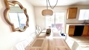 A dining area with a wooden table and white chairs, a large mirror, and a hanging light fixture. - Luxe 5 BR Family Friendly Oasis-5 King Beds-Hot Tub-Fire Pit-Ski-Hike-Yard Games (Sandy)