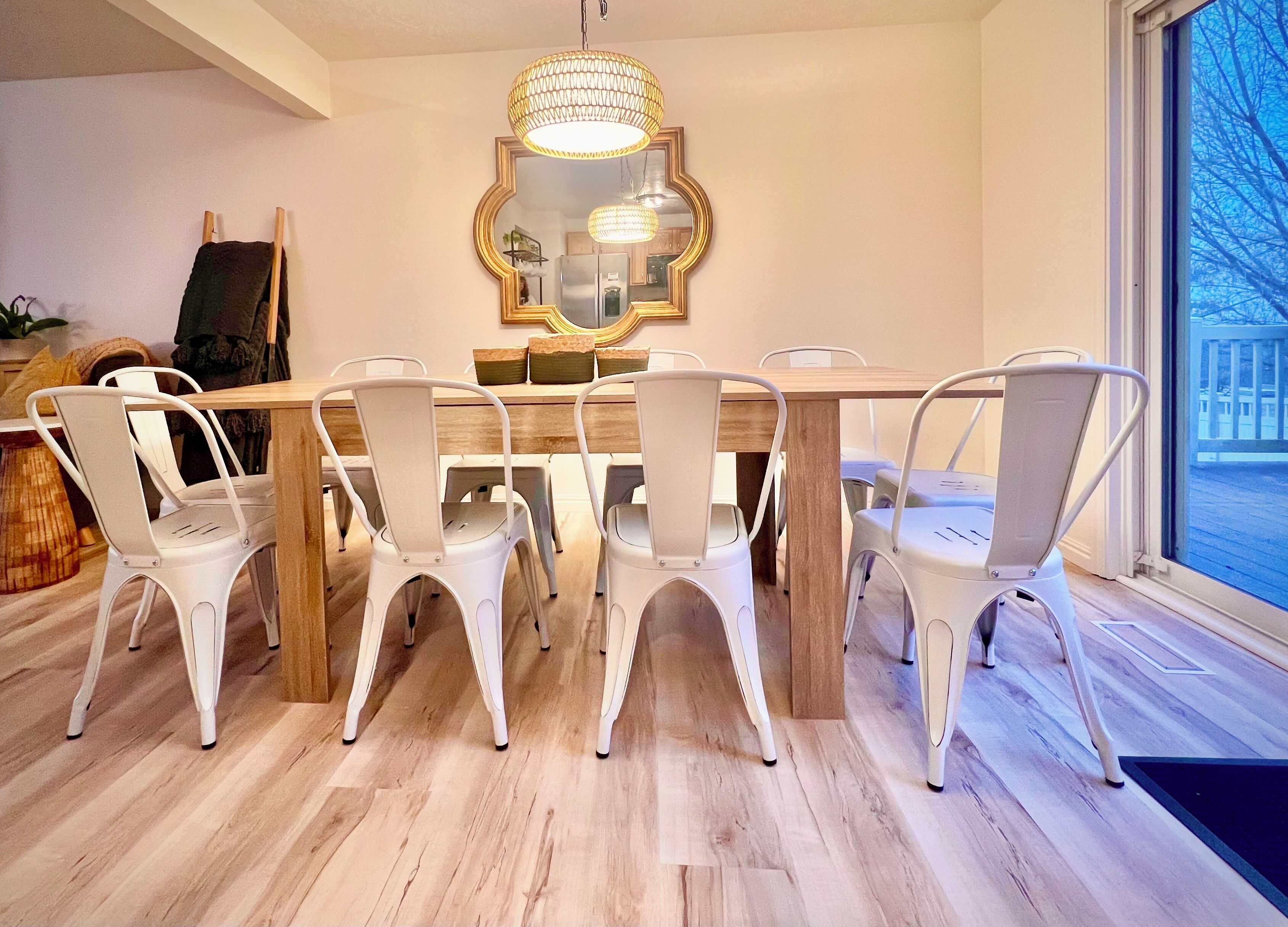 Un coin repas avec une table en bois et des chaises blanches, un grand miroir et une fenêtre donnant sur un beau paysage.