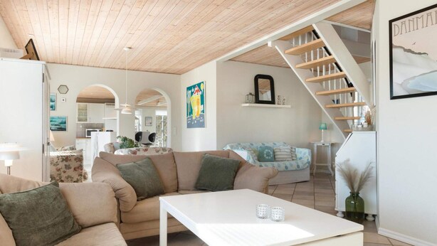 A modern living room with a wooden ceiling, a staircase, and a dining area. - 5 Star Holiday Home in Lokken (Lokken)
