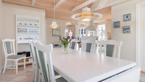 A spacious dining area with a white table and chairs, wooden ceiling beams, and pendant lighting. - 5 Star Holiday Home in Lokken (Lokken)