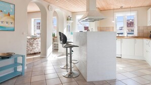 A spacious kitchen with white cabinets, a central island, and a wooden ceiling. - 5 Star Holiday Home in Lokken (Lokken)
