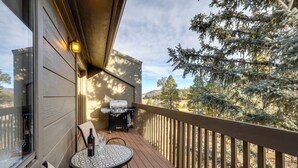 A balcony with a grill, a table with a bottle and glass, and a view of trees and mountains. - Cozy Flagstaff Condo in Country Club Community! (Flagstaff)