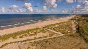 A coastal landscape with a sandy beach, grassy dunes, and a clear sky with clouds. - Holiday Home in Petten With Garden (Petten)