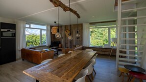 A modern kitchen with a wooden table, white chairs, and a built-in oven. - Holiday Home in Petten With Garden (Petten)