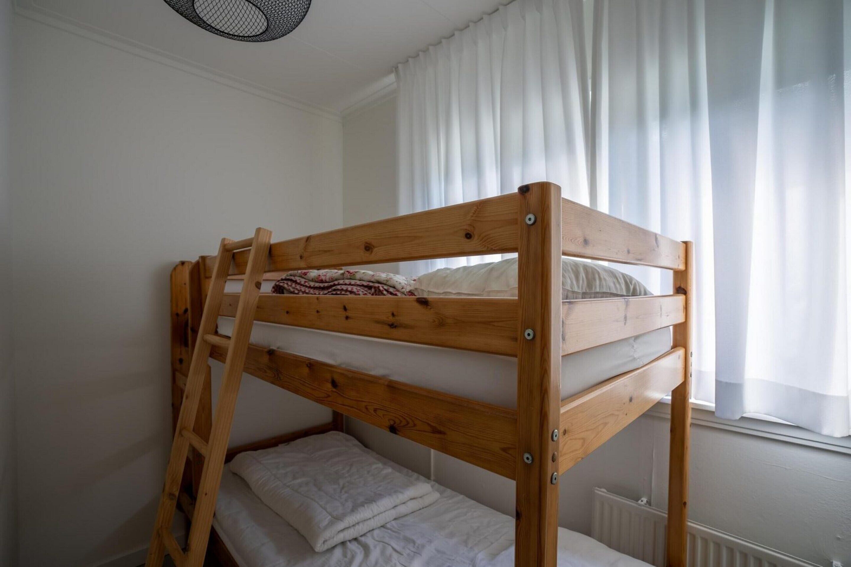 A bunk bed with a wooden frame, a ladder, and a white mattress.