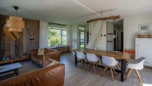 A modern living room with a wooden dining table, white chairs, and a brown leather sofa. - Holiday Home in Petten With Garden (Petten)