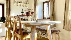 Un comedor con una mesa y sillas de madera, una lámpara colgante y una repisa con utensilios de cocina.