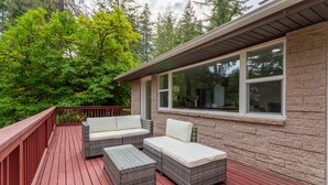 A covered deck with wicker furniture and a stone exterior wall.