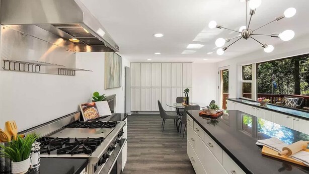 A modern kitchen with a gas stove, stainless steel range hood, and a dining area with a glass table and chairs.