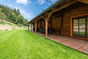 A wooden cabin with a covered patio, outdoor seating, and a view of a forested hillside.