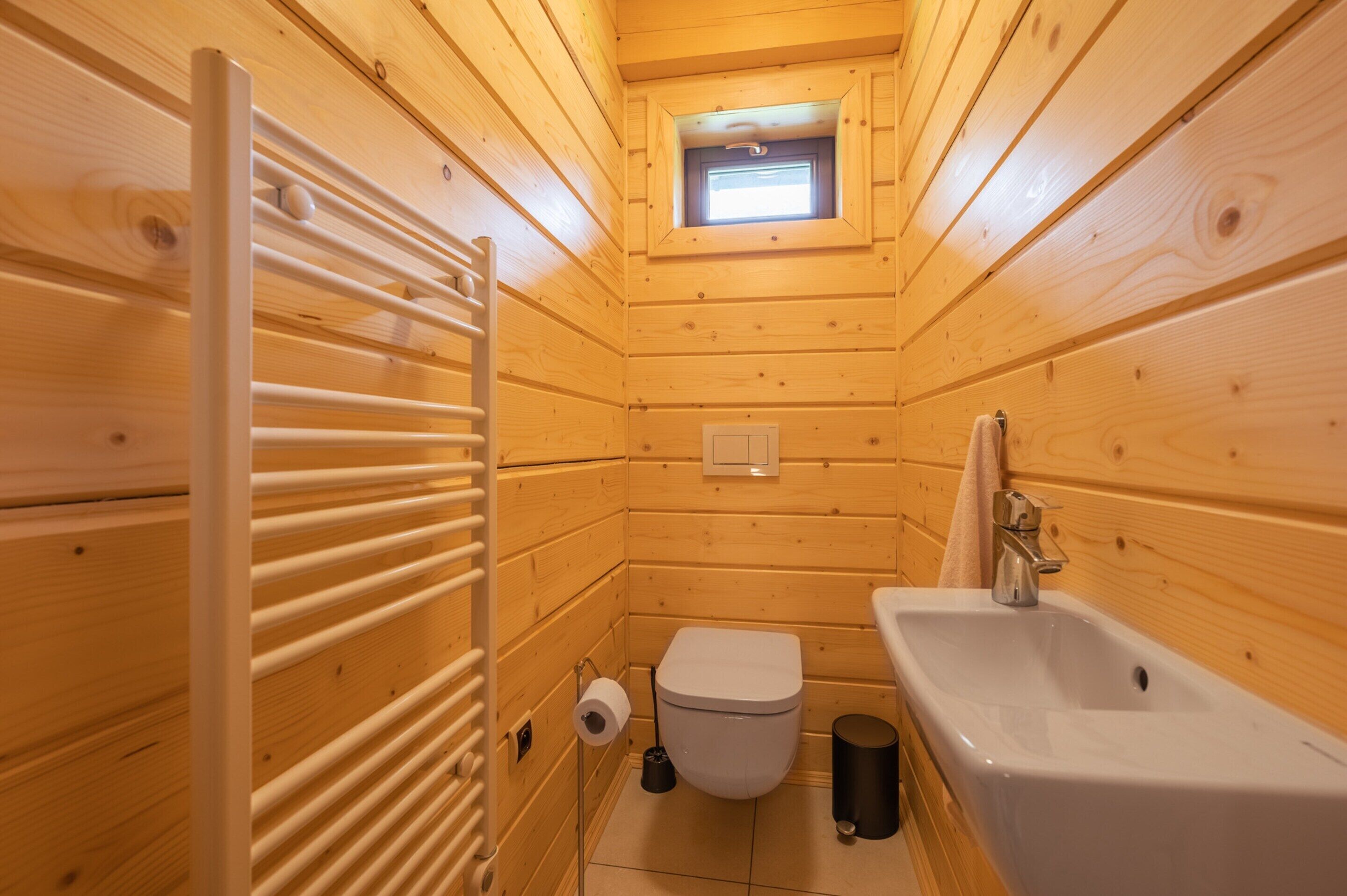 Ein kleines Badezimmer in einer Holzblockhütte mit Toilette, Waschbecken und einem kleinen Dachfenster.