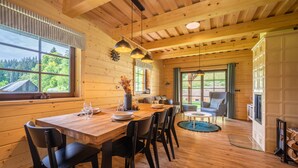 A wooden interior with a dining table set for four, a fireplace, and large windows offering a view of the outdoors. - Tranquil Villa in Velke Karlovice (Velké Karlovice)