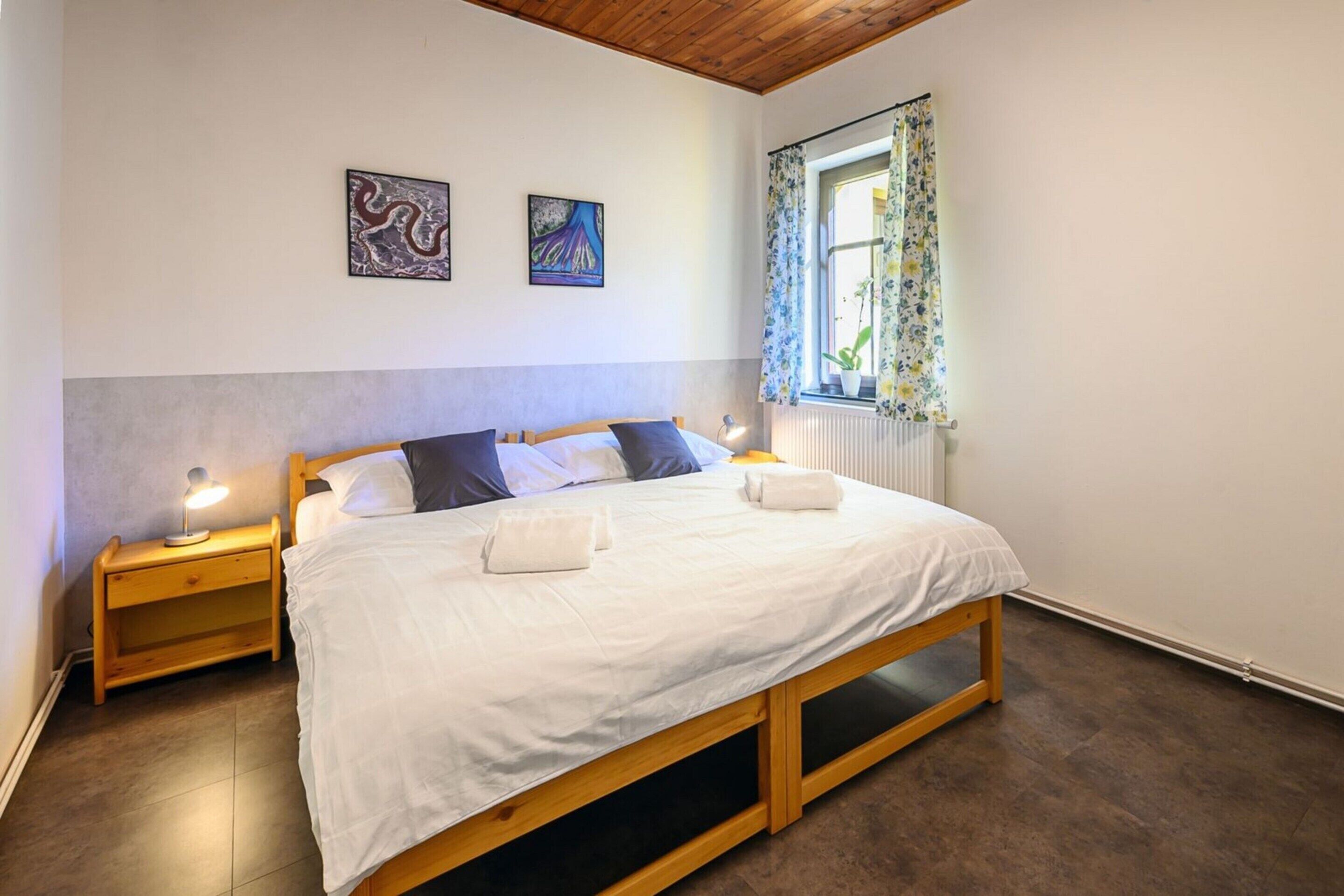 A bedroom with a wooden bed, two bedside tables with lamps, a radiator, and two wall-mounted artworks.