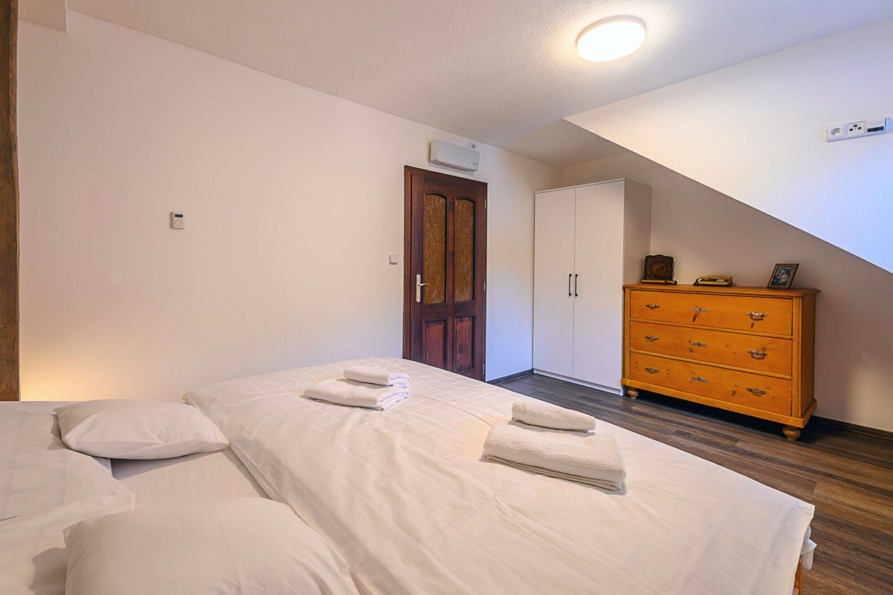 A bedroom with two beds, a wooden dresser, a wardrobe, and an air conditioning unit.