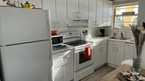 Una cocina moderna con armarios blancos, un refrigerador, un horno, un lavamanos y una cafetera.