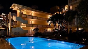 Una piscina de noche con un edificio al fondo.