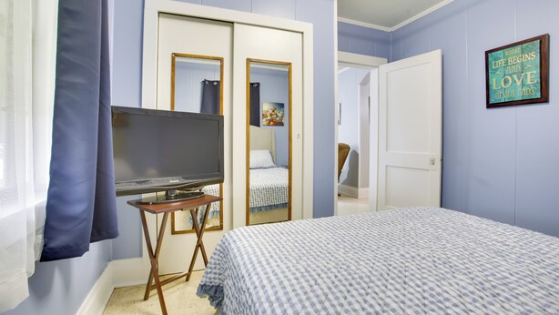 A bedroom with a bed, a television on a stand, a wardrobe, and a door leading to another room. - Walk to 1st Street: Family Home in Thibodaux! (Thibodaux)
