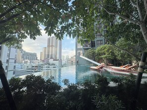Piscina no terraço com espreguiçadeiras, cercada por áreas verdes e edifícios modernos.
