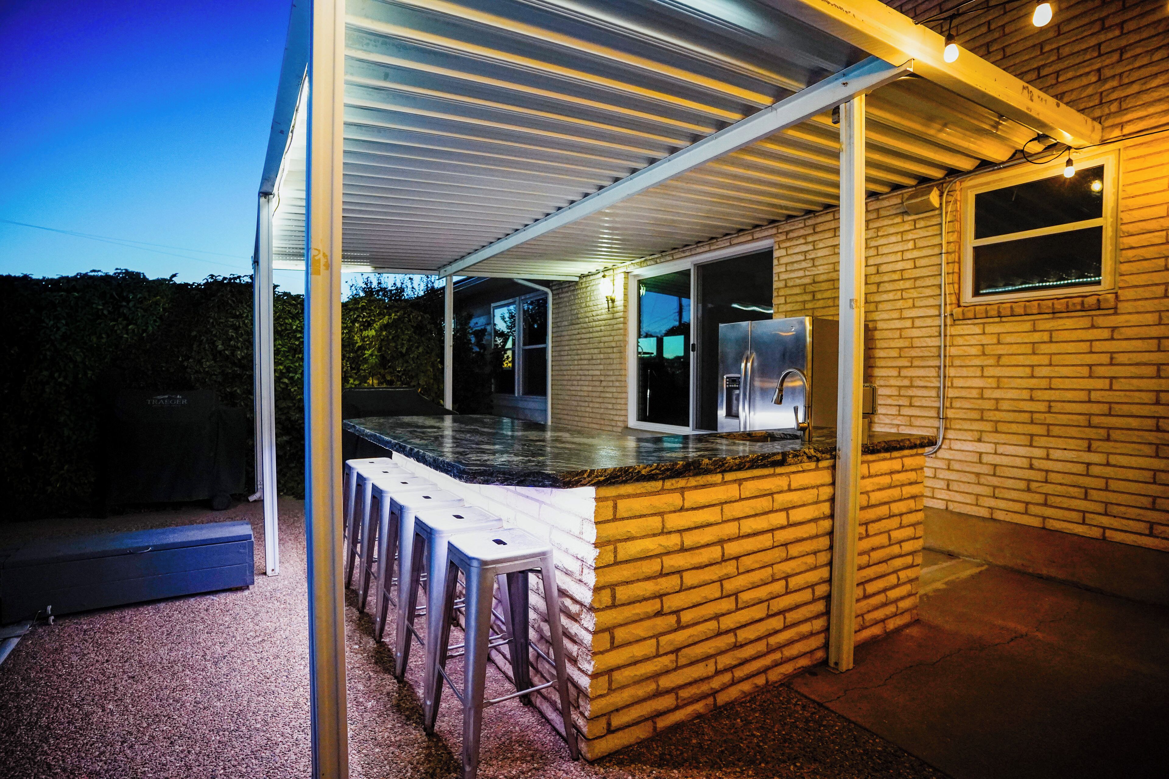 Un espace cuisine extérieur abrité, doté d’un mur en briques, d’un réfrigérateur en acier inoxydable et d’un tabouret de bar.