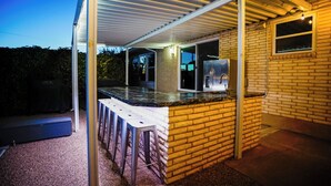 A covered outdoor kitchen area with a brick wall, a stainless steel refrigerator, and a bar stool. - Pool & Hot Tub Access: Luxury Roy Oasis! (Roy)