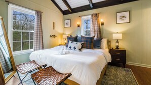 A bedroom with a large bed, two bedside tables with lamps, a bench, and a window with curtains.