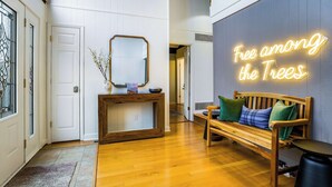 A wooden bench with cushions, a console table with a mirror, and a neon sign reading "Free among the Trees."