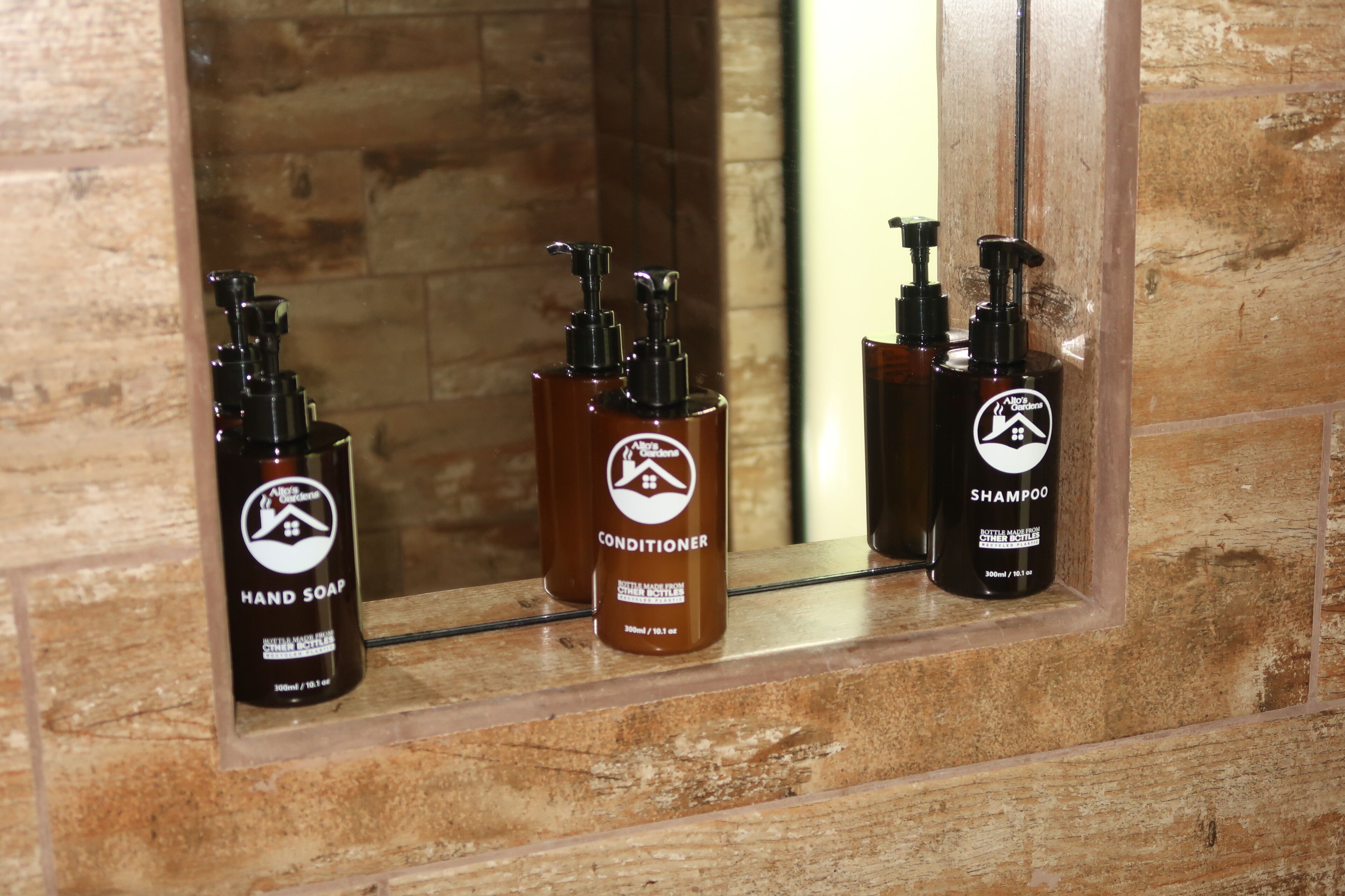 Three bottles of hand soap, conditioner, and shampoo on a shelf in a bathroom with a wooden wall.
