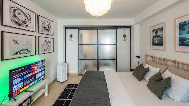 A modern hotel room with a large bed, a flat-screen TV, artwork on the walls, and a large window with a view. - Stylish 3 Bd 3 Bath Duplex In Brussels (Brussels)