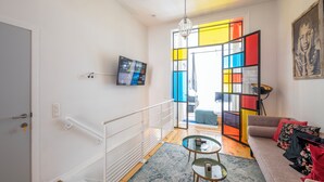 A modern living room with a staircase, a television, a colorful partition, and a sofa with cushions. - Stylish 3 Bd 3 Bath Duplex In Brussels (Brussels)