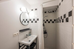 Bathroom features a sink, mirror, shower with handheld showerhead, and a checkered-patterned wall.