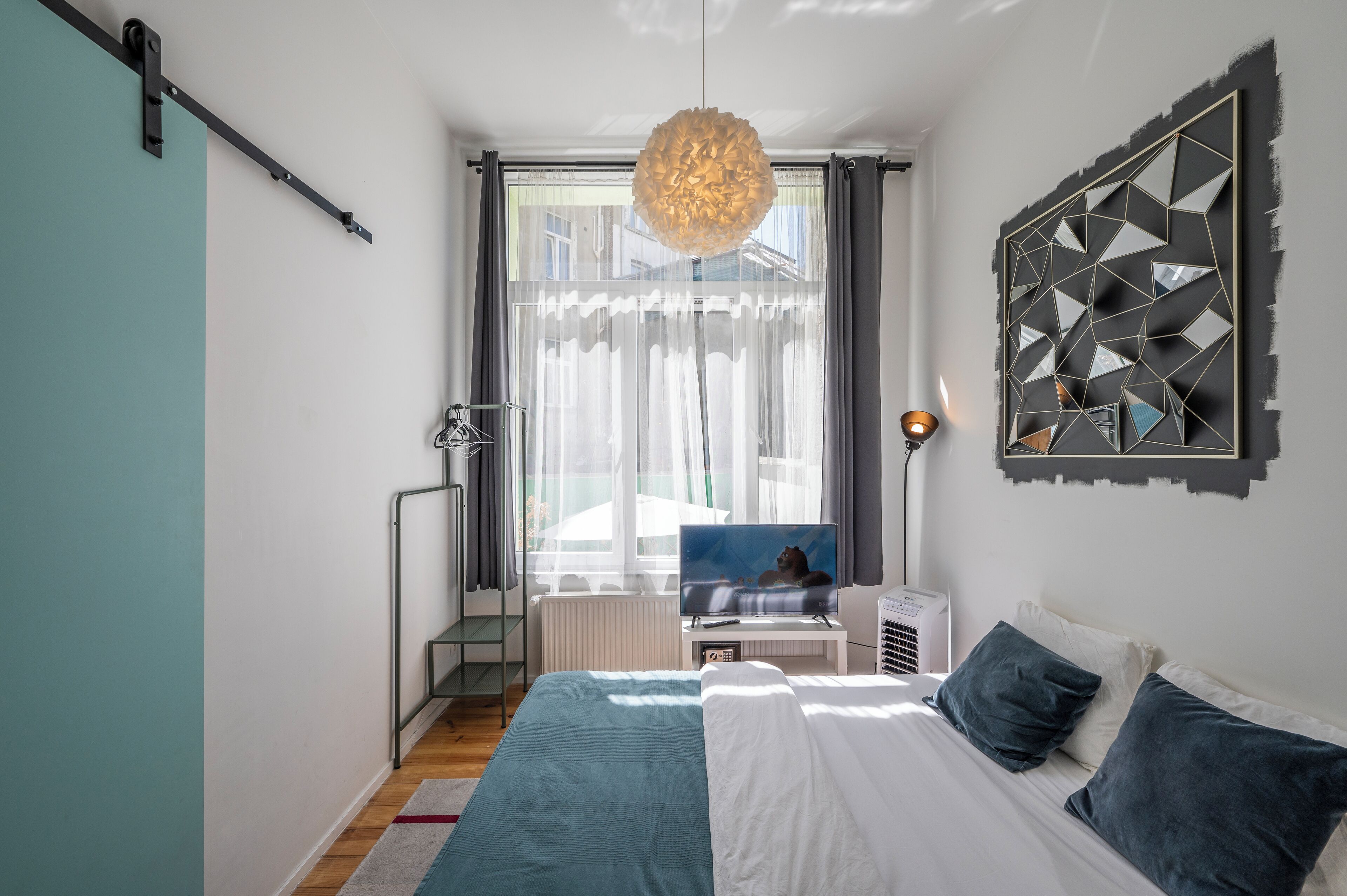 Un dormitorio moderno con una cama, un televisor, una lámpara colgante y una obra de arte geométrica en la pared.
