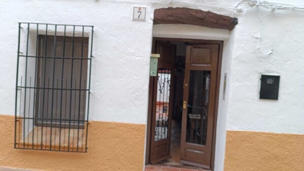 Un edificio con fachada blanca y amarilla, una ventana con rejas y una puerta con panel de vidrio.
