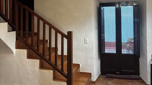 Eine Treppe mit Holzwerteln führt zu einer Zwischenebene, mit Deckenventilator, einer Tür mit Fenster und einer Leuchte.
