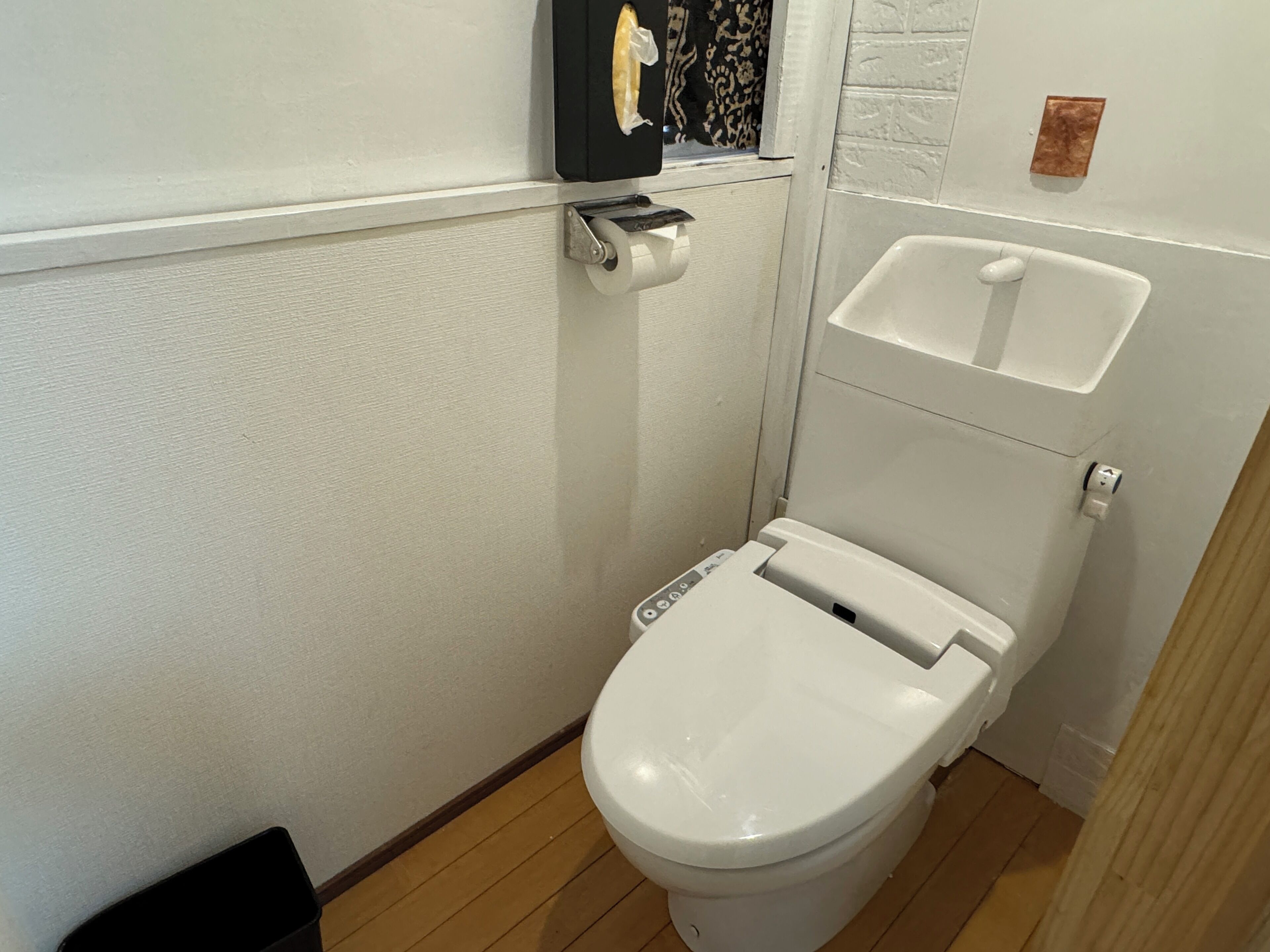 A small, white toilet with a control panel, a white sink, and a wooden floor.