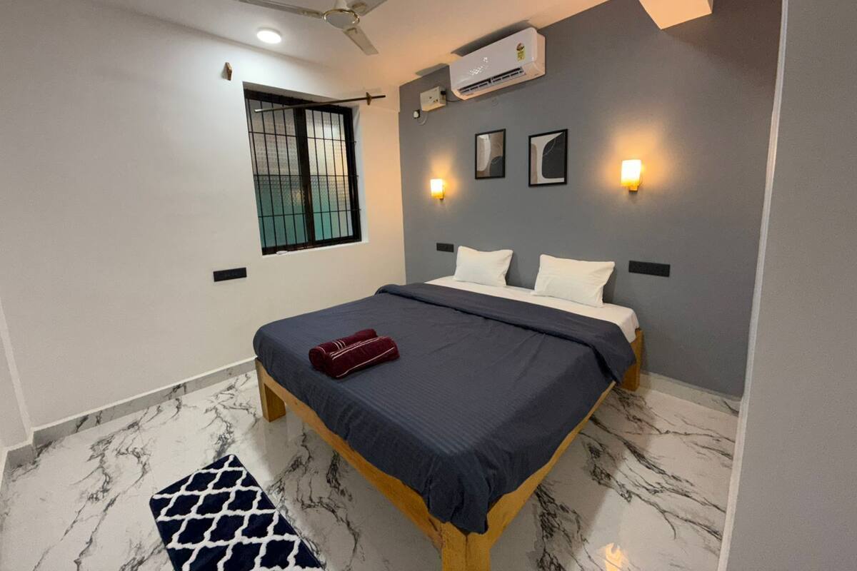 Une chambre à coucher avec un lit, un ventilateur de plafond, un appareil de climatisation et une fenêtre avec des barreaux.
