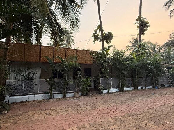A building with a brick facade, surrounded by a paved courtyard with palm trees and a fence.