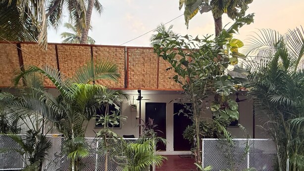 A courtyard with a building entrance, surrounded by potted plants and a stone pathway. - The Village Harmony by Red Rose (Canacona)