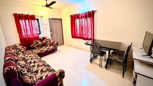 A living room with a sofa, a dining table with chairs, a ceiling fan, and a TV. - The Village Harmony by Red Rose (Canacona)