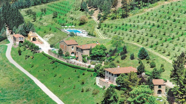 An aerial view of a rural property with multiple stone buildings, a swimming pool, and terraced fields.
