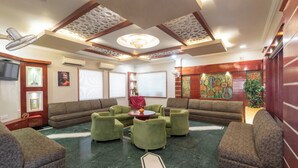 A spacious living room with a green carpet, multiple sofas, a round coffee table, and a decorative ceiling. - DLS Park Grace (Haridwar)